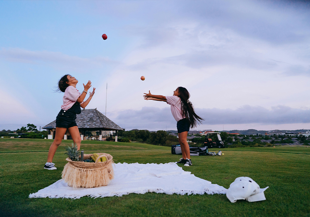 Two young girls throwing balls in the sky in a park. 